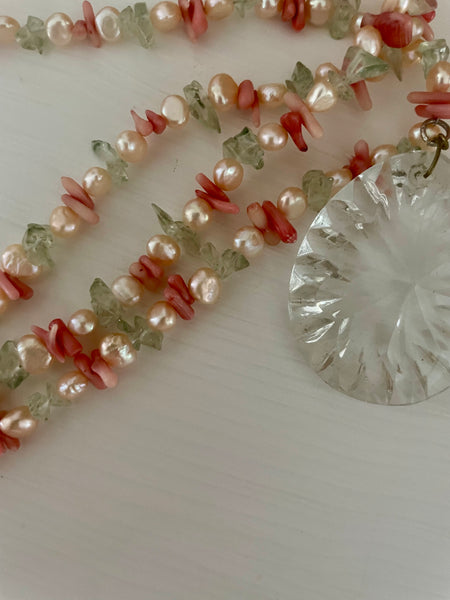 Necklace with pink and green beads and a clear pendant on a white background